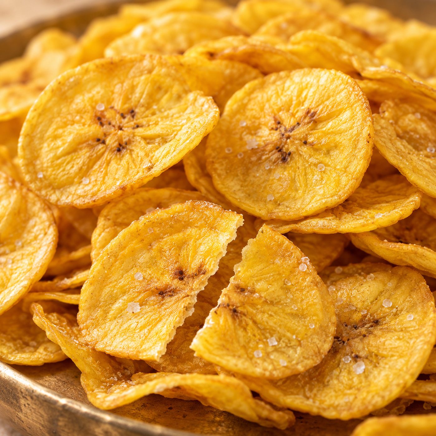 Close-up of thin golden Kerala banana chips with salt crystals, one snapped in half.