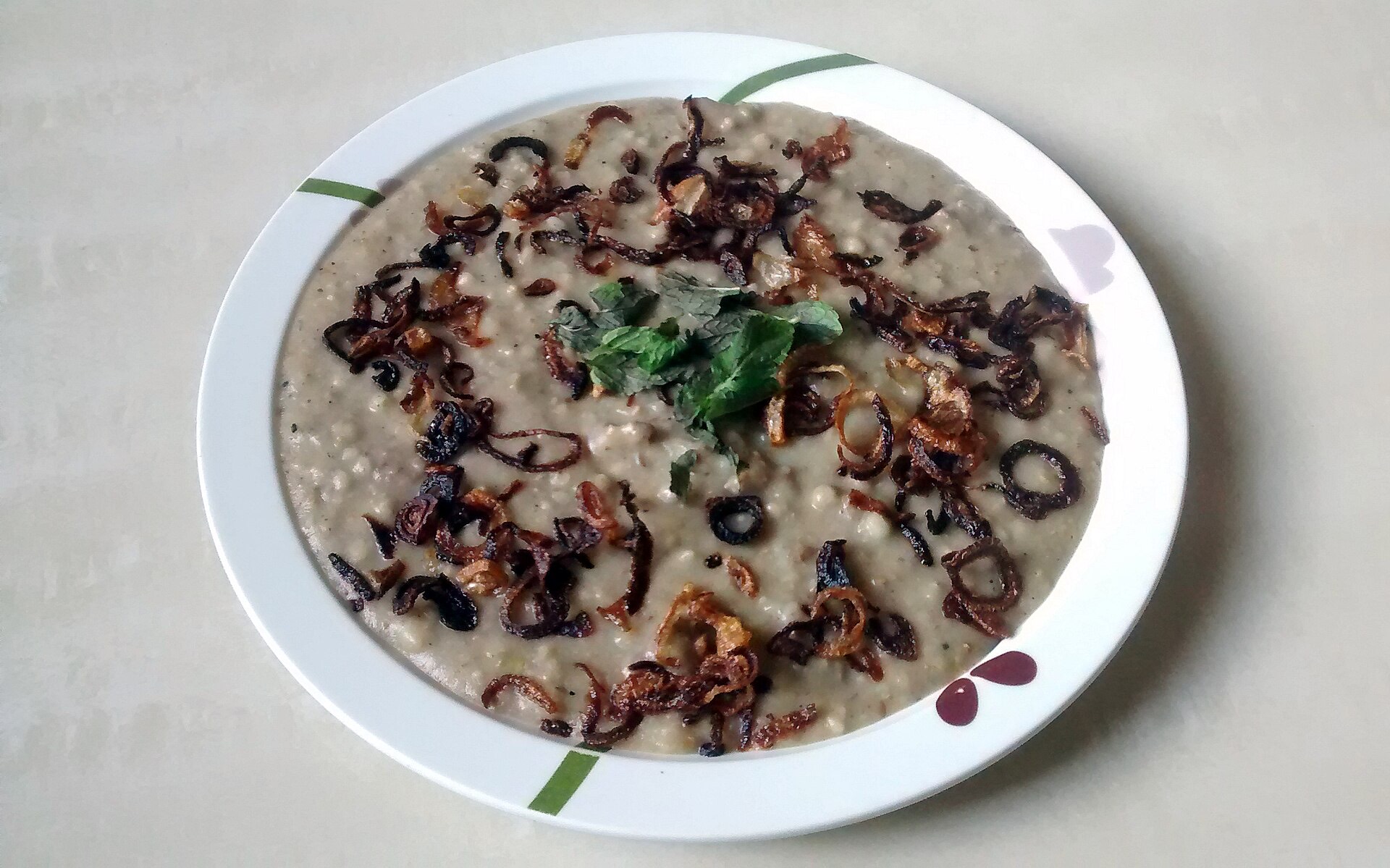 A bowl of Aleesa, the smooth Malabar wheat-and-chicken porridge, topped with fried shallots, cashews and ghee.