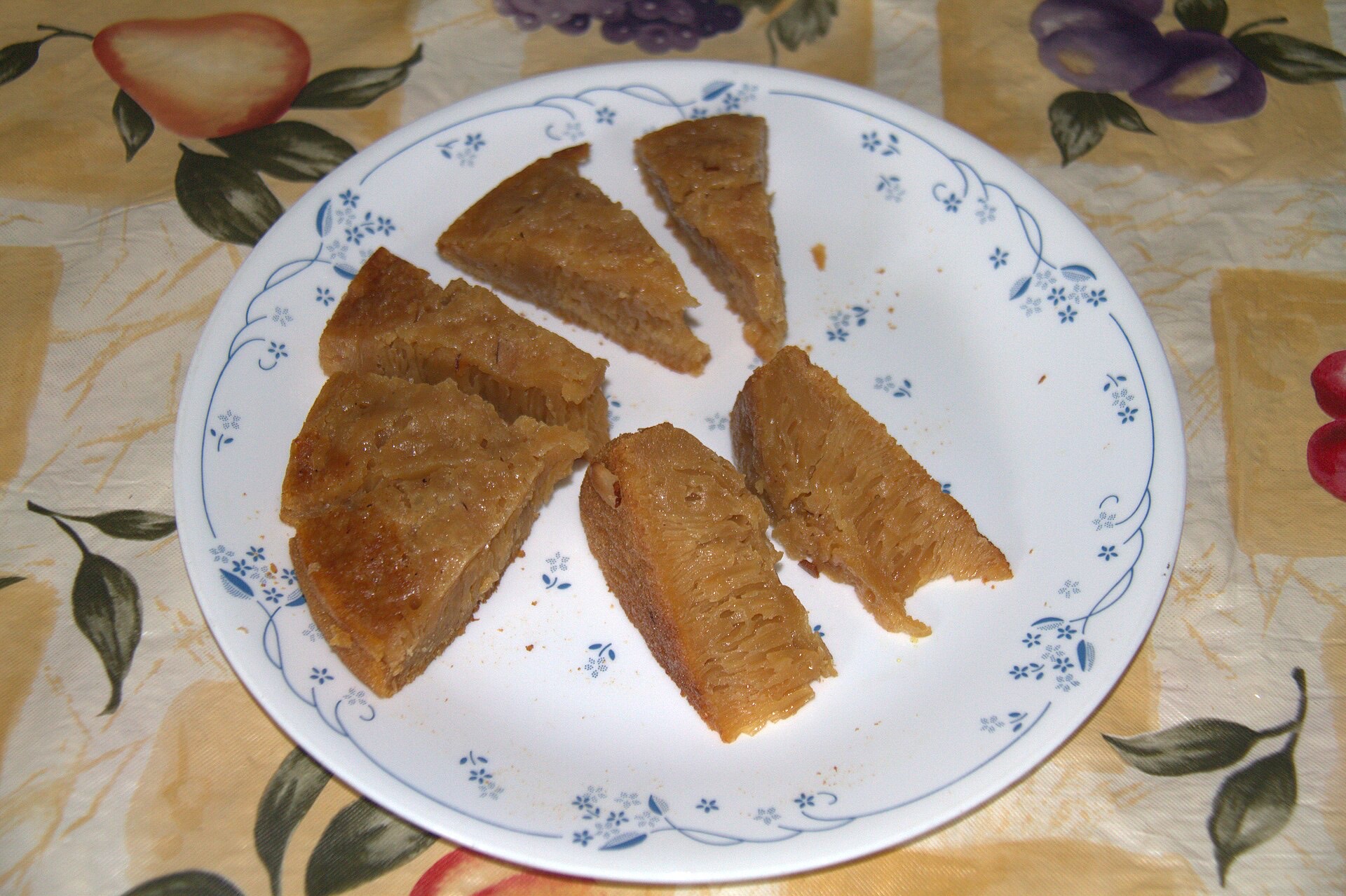 A wedge of dark Kalathappam, the Malabar rice-and-jaggery cake, showing coconut and shallot pieces.