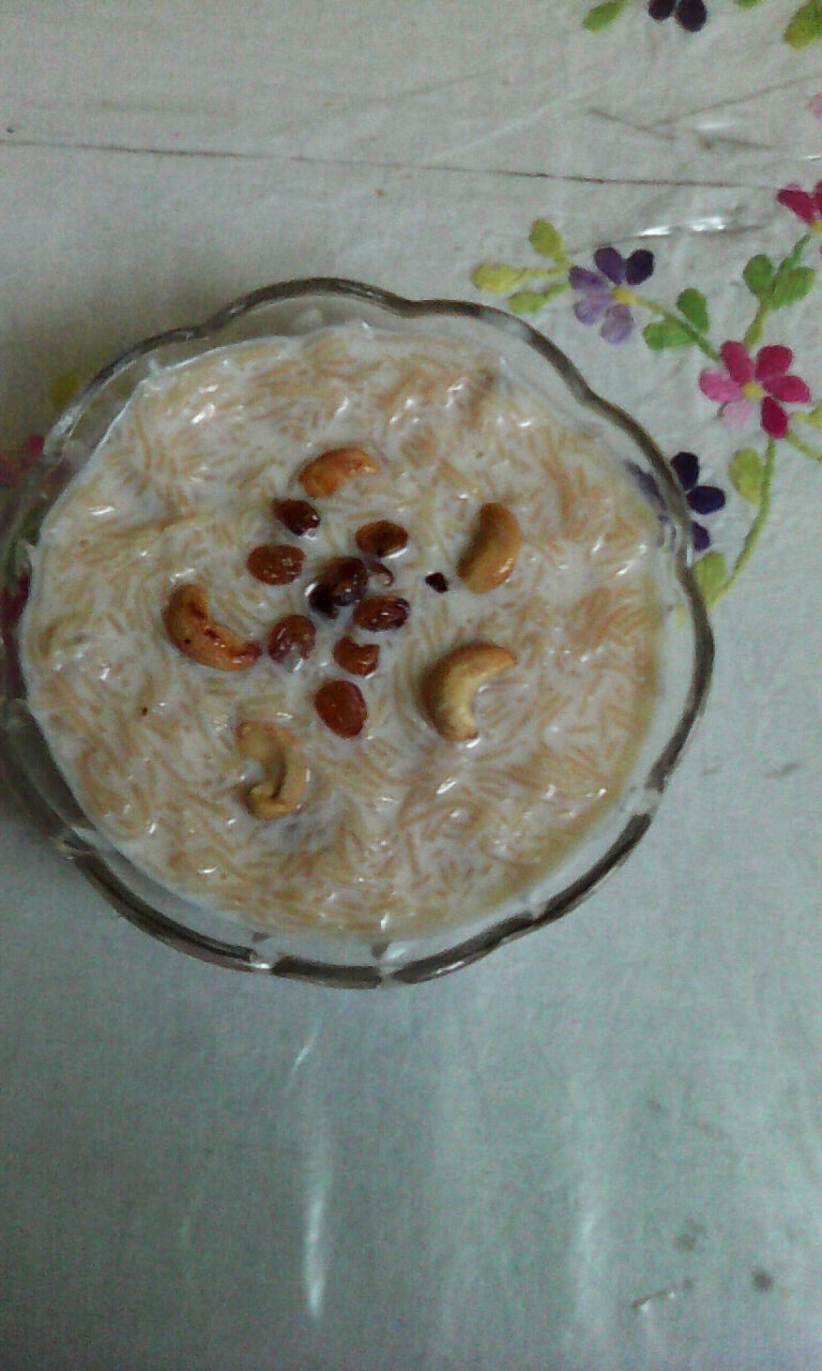A glass of warm Thari Kanji, the Malabar sweet semolina drink, topped with cashews and raisins.